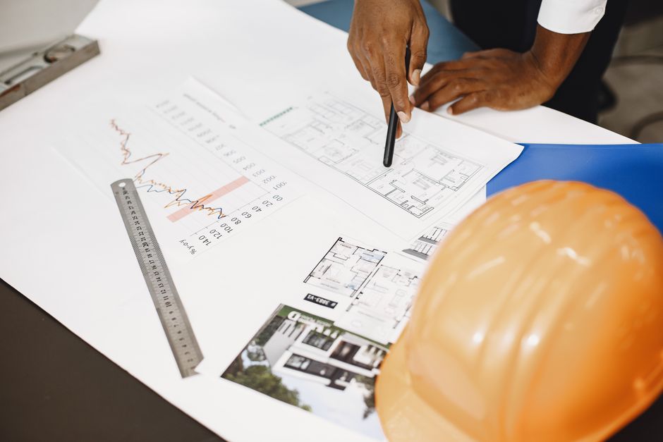A person reviews a detailed plan and tools on a desk.