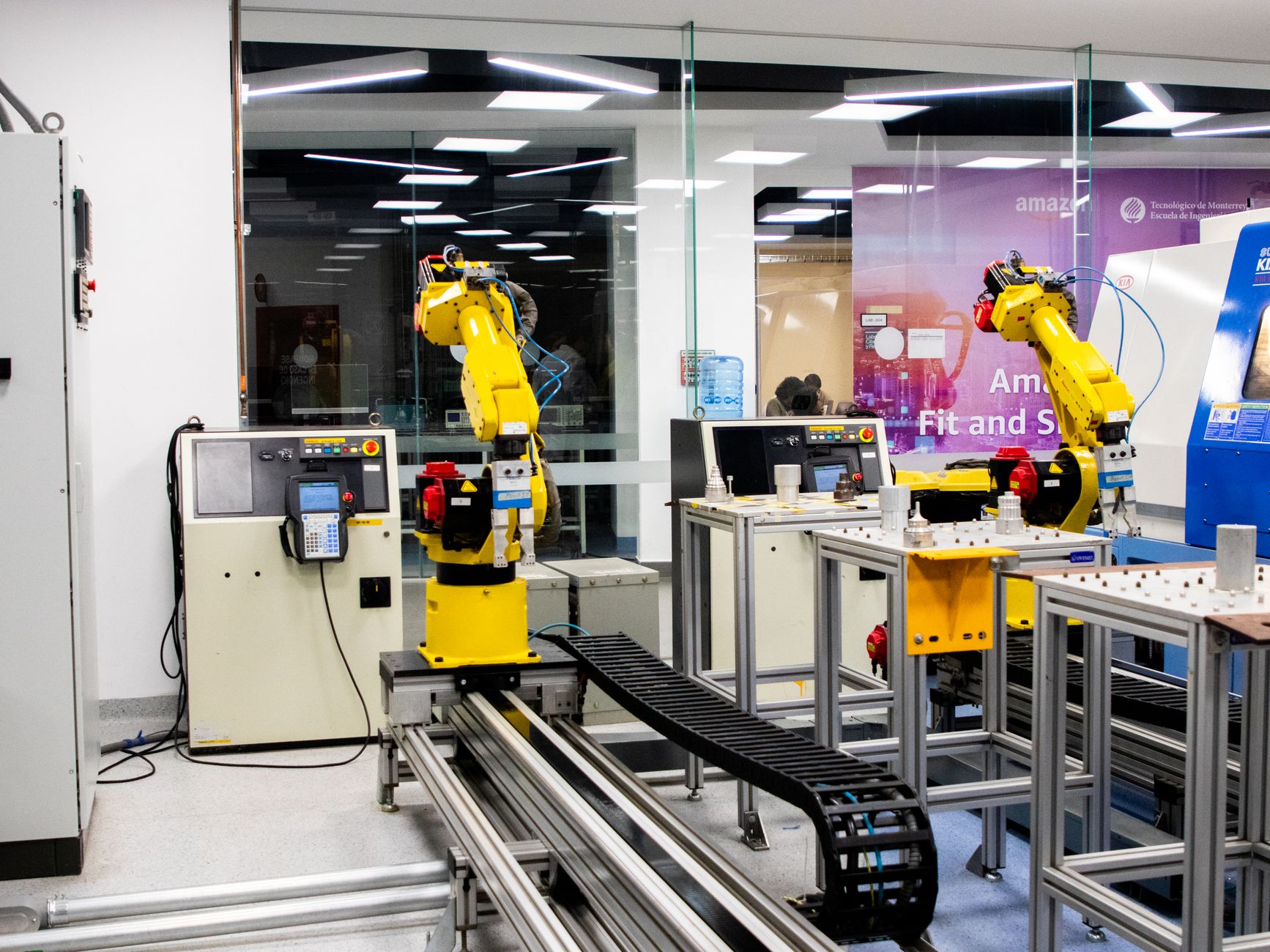 Two identical yellow robotic arms mounted on parallel rails in an automation lab, each working its own station off the same track