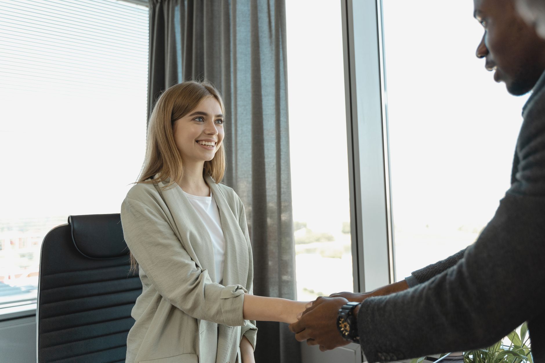 A job candidate sitting across a small table from two interviewers in a bright office, mid-sentence with hands open