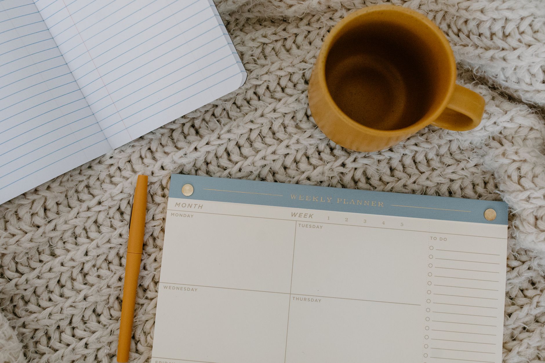 Flat lay of a planner, notebook, and coffee mug on a knitted blanket for a cozy planning session.