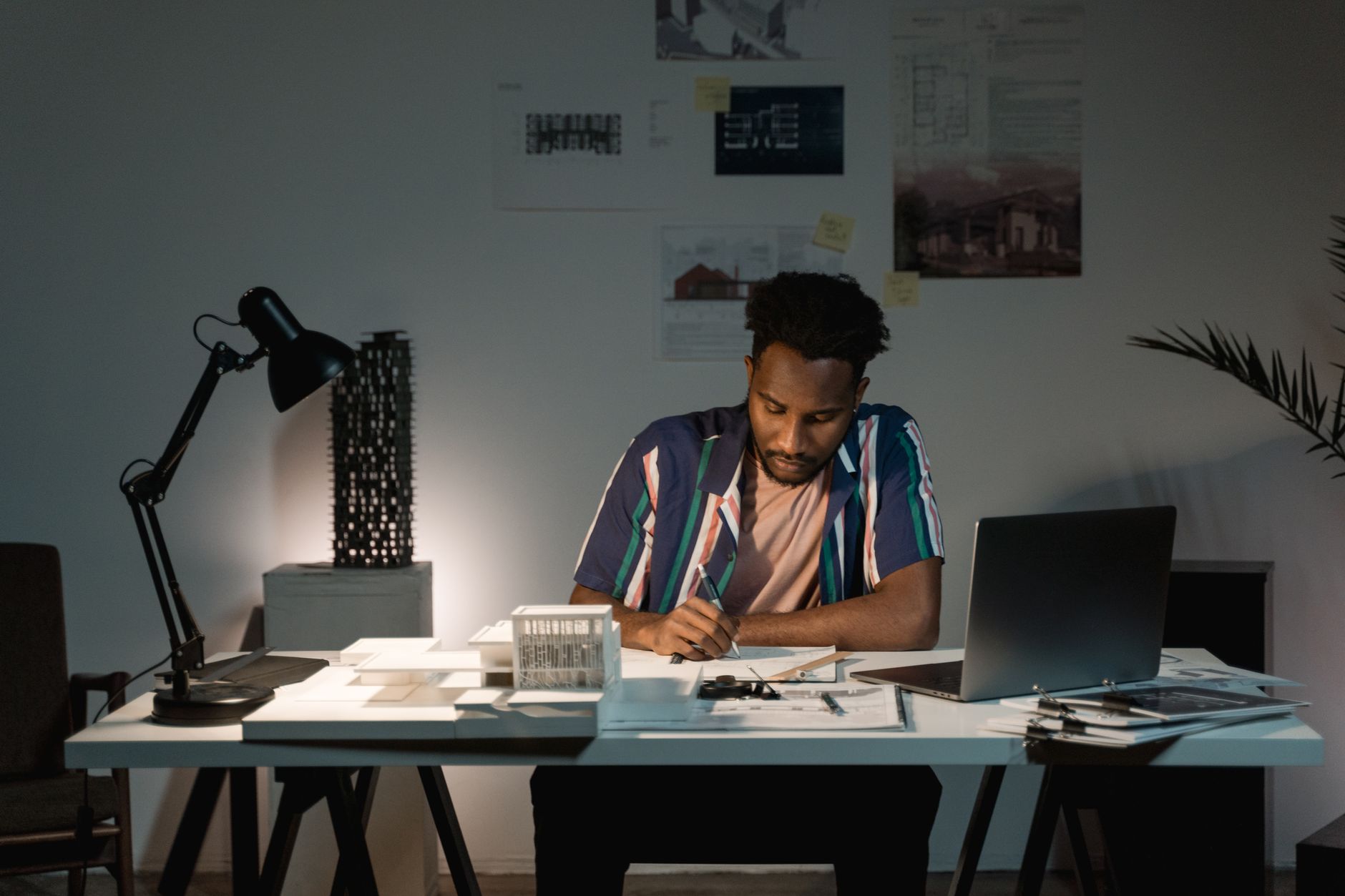 An African American man intensely working at his office desk in low light, surrounded by documents.